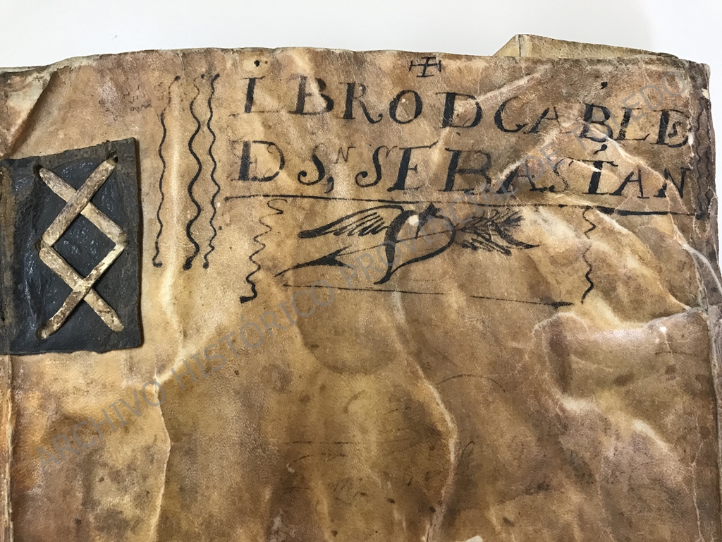 Imagen parcial de un pergamino, con refuerzos en cuero, con un dibujo de un corazón alado y, sobre él, la inscripción "Libro de cabildos de San Sebastián".